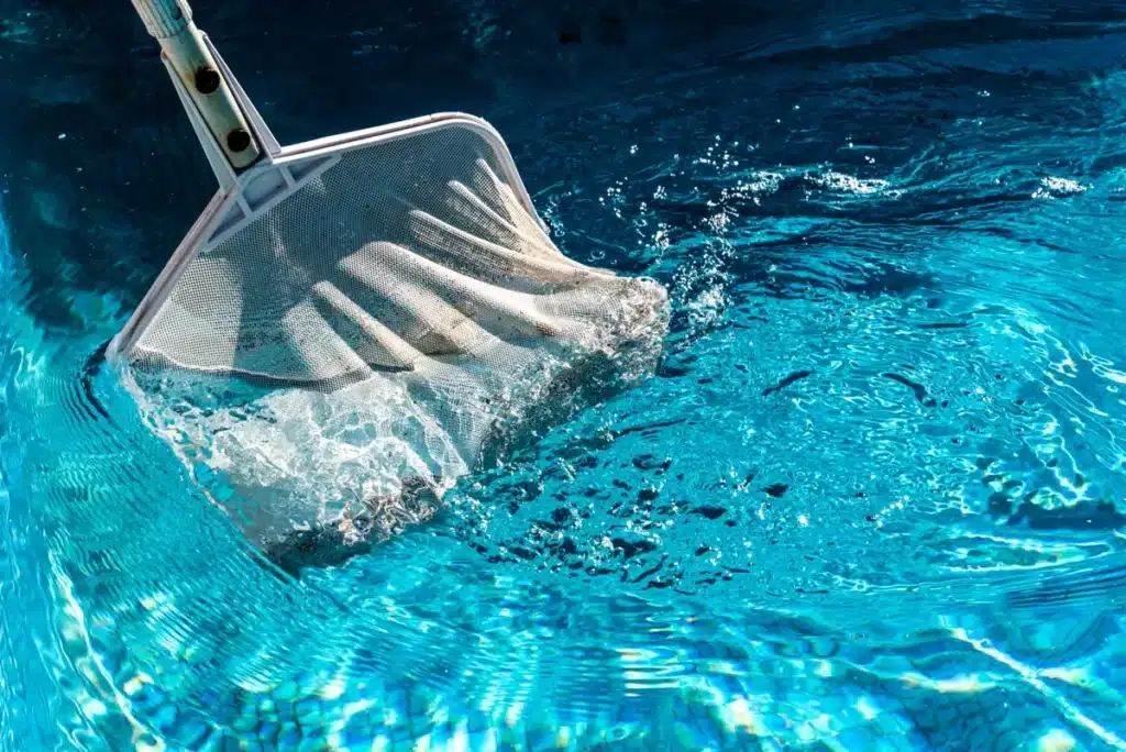 Nettoyage d'une piscine avec une épuisette, illustrant l'entretien professionnel proposé par un pisciniste qualifié.